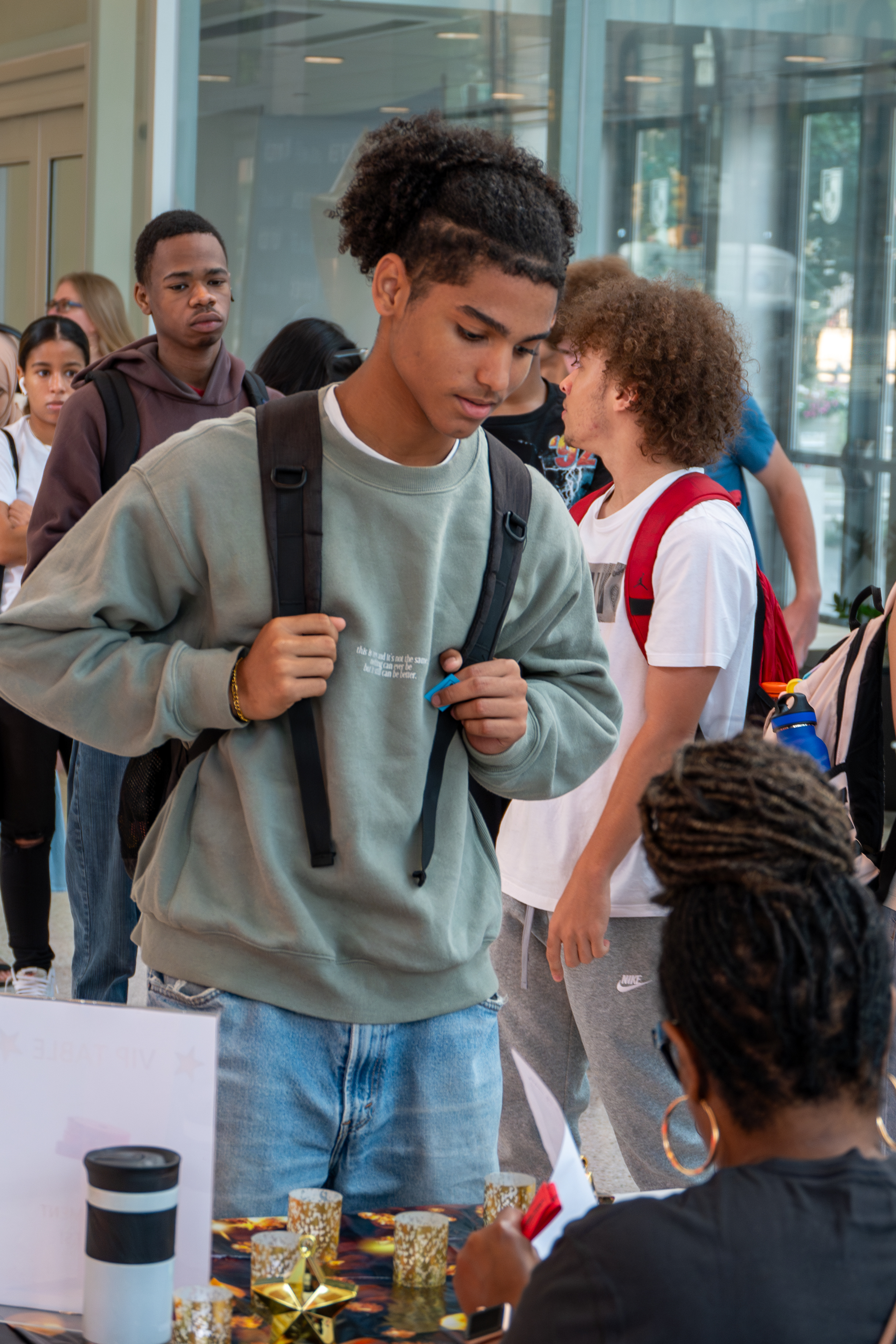 A student stands in front of a table talking and checking in with a staff member.